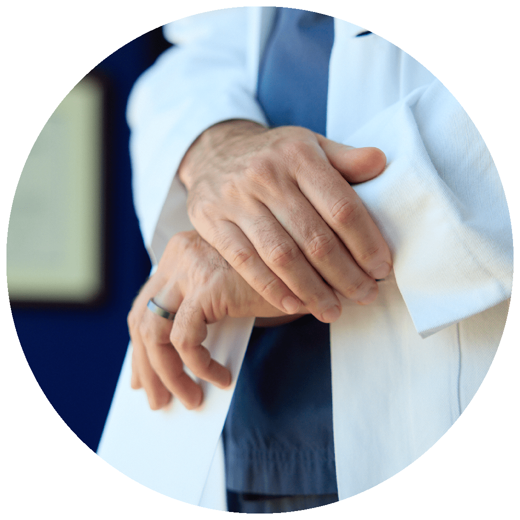 Close-up of a doctor wearing a white coat over scrubs with crossed hands.