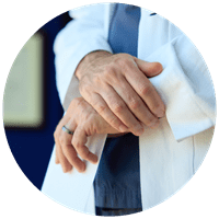 Close-up of a doctor wearing a white coat over scrubs with crossed hands.