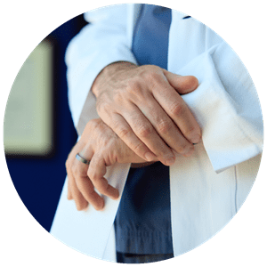 Close-up of a doctor wearing a white coat over scrubs with crossed hands.