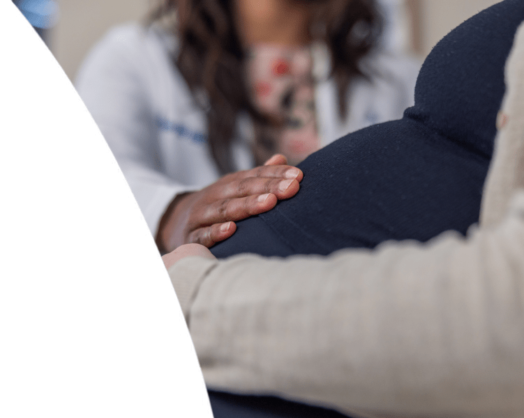 A doctor placing her hand gently on a pregnant woman's abdomen.