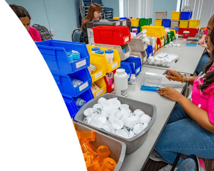 Healthcare workers organizing medications and supplies using colorful sorting bins and prescription bottles.