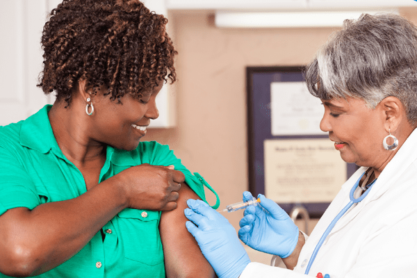 Healthcare provider administering a vaccine to an adult patient during an immunization appointment, with both smiling in a clinical setting.