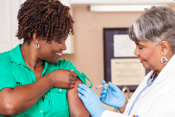 Healthcare provider administering a vaccine to an adult patient during an immunization appointment, with both smiling in a clinical setting.